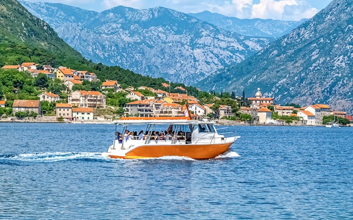 Speedboat on Kotor Bay with coastal village and mountains in Montenegro.