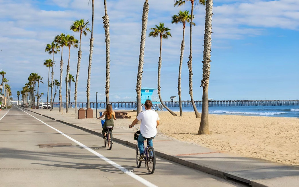 Cyclists on a beachside path with palm trees and ocean view in San Diego.