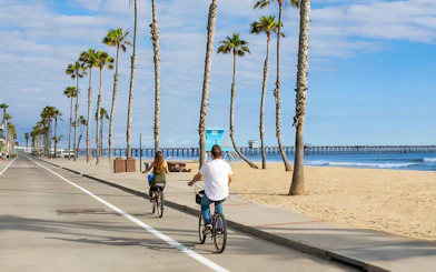 Cyclists on a beachside path with palm trees and ocean view in San Diego.