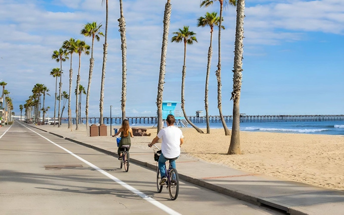 Cyclists on a beachside path with palm trees and ocean view in San Diego.