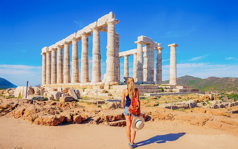 Visitor at the Temple of Poseidon, Greece, with ancient columns and scenic landscape.