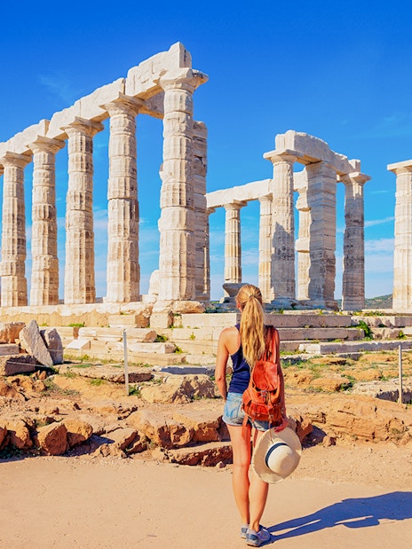 Visitor at the Temple of Poseidon, Greece, with ancient columns and scenic landscape.