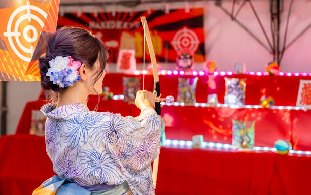 Person in yukata aiming a bow at a target during NAKED Summer Festival 2024 at Nijo-jo Castle.