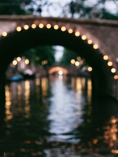 Evening canal view with lit bridge in Amsterdam, captured on a smartphone during a luxury cruise.