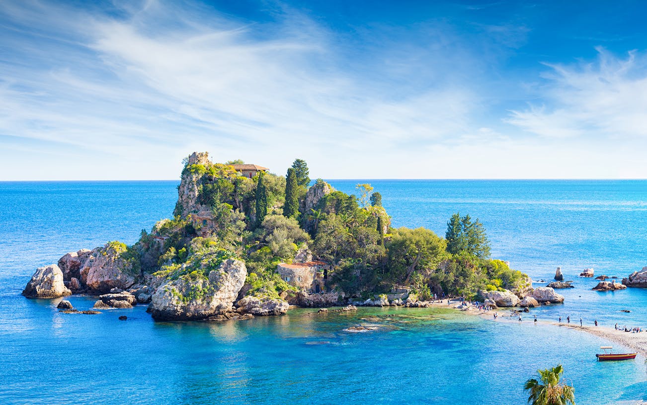 Taormina Island with lush greenery surrounded by blue sea and rocky coastline.