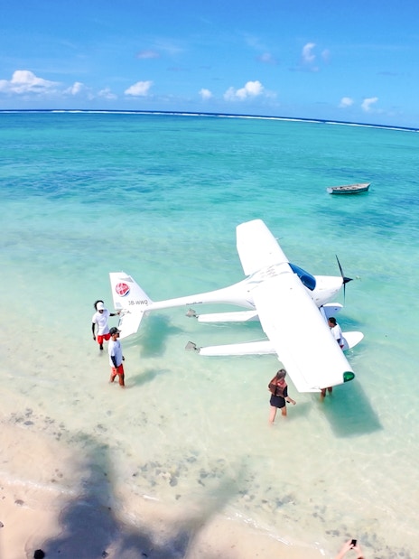 Seaplane on turquoise waters with people on a beach in Mauritius.