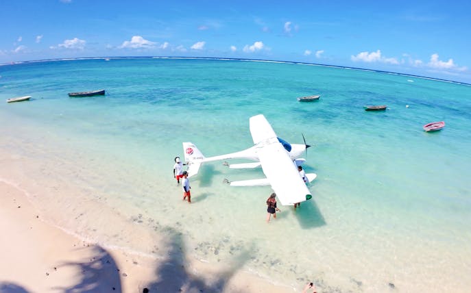 Seaplane on turquoise waters with people on a beach in Mauritius.