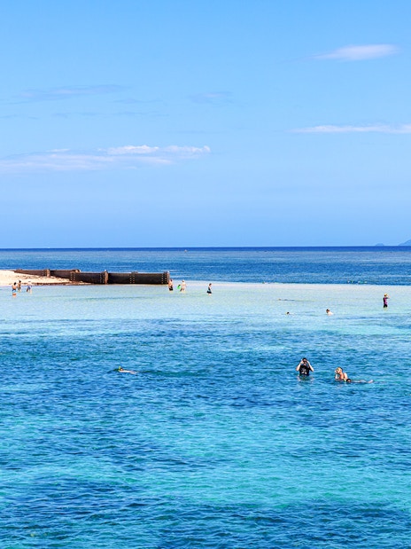 Snorkelers exploring clear waters near a sandy beach with distant islands.