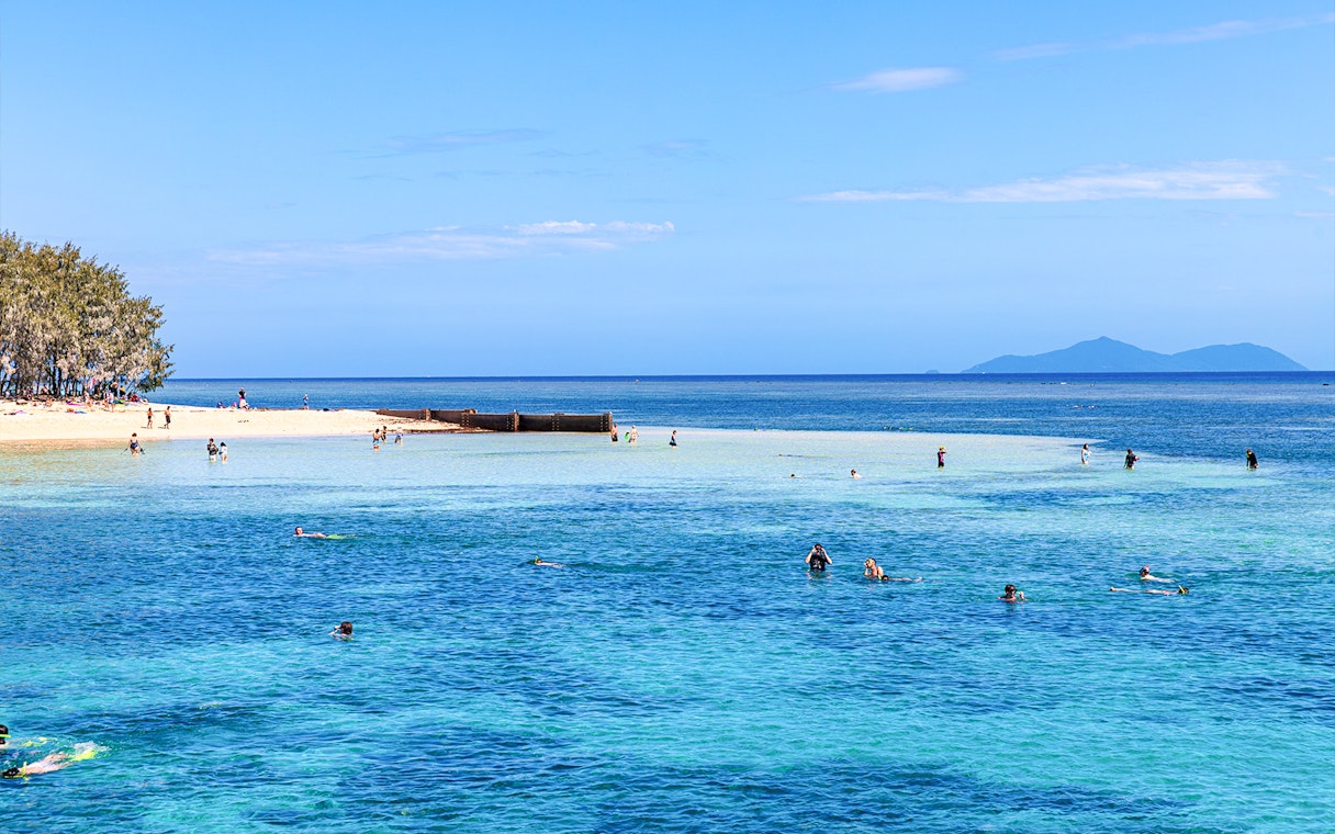 Snorkelers exploring clear waters near a sandy beach with distant islands.