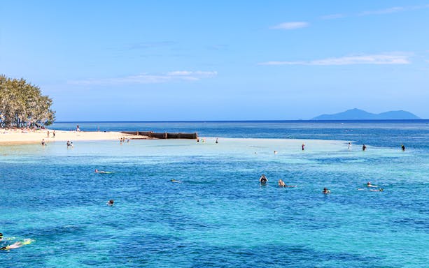 Snorkelers exploring clear waters near a sandy beach with distant islands.