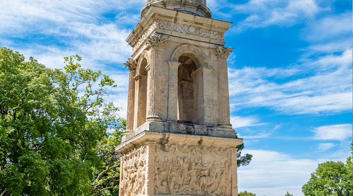 Ancient mausoleum at the archaeological site of Glanum, France, surrounded by trees.