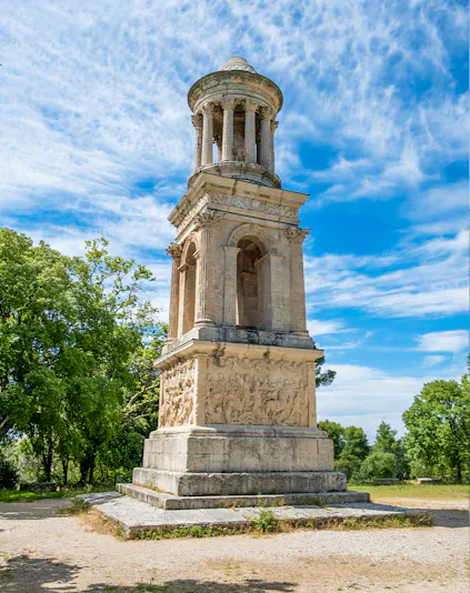 Ancient mausoleum at the archaeological site of Glanum, France, surrounded by trees.