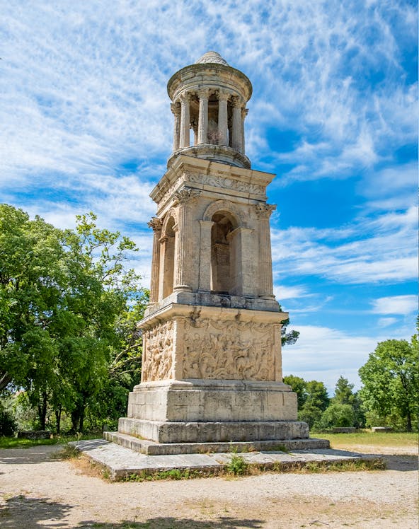 Ancient mausoleum at the archaeological site of Glanum, France, surrounded by trees.
