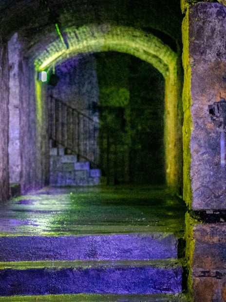 Dimly lit stone corridor in Edinburgh's Terror Tour with arched ceiling and stairs.