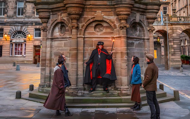 Tour guide in historical costume leading a group on a daytime underground ghost tour in a city square.