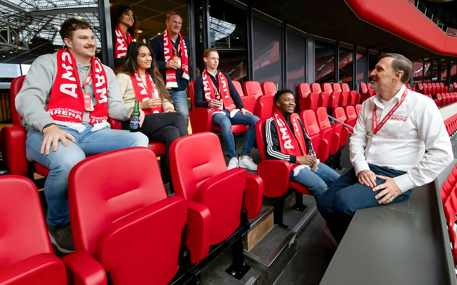 Visitors on a VIP tour at Johan Cruijff ArenA, Amsterdam, holding drinks and scarves.