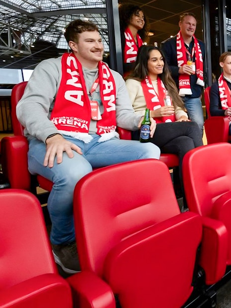 Visitors on a VIP tour at Johan Cruijff ArenA, Amsterdam, enjoying drinks and wearing scarves.
