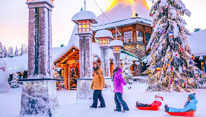 Guided tour at Santa Claus Village Rovaniemi with children sledding in snow.