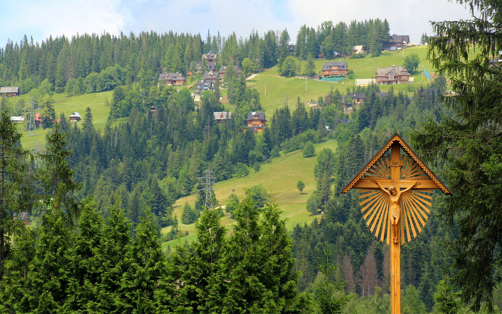 Wooden crucifix in a lush green landscape near Zakopane, Poland, with hillside homes in the background.