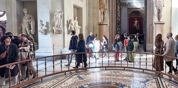 Visitors exploring the Round Hall in the Vatican Museums, Rome, with ancient statues and mosaic floor.