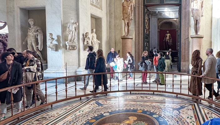 Visitors exploring the Round Hall in the Vatican Museums, Rome, with ancient statues and mosaic floor.