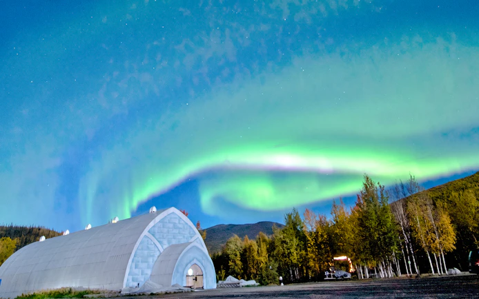 Northern lights over Chena Hot Springs ice museum with forest backdrop.