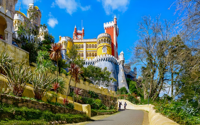 Pena Palace in Sintra with colorful towers and a winding path lined with greenery.