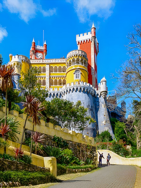 Pena Palace in Sintra with colorful towers and a winding path lined with greenery.