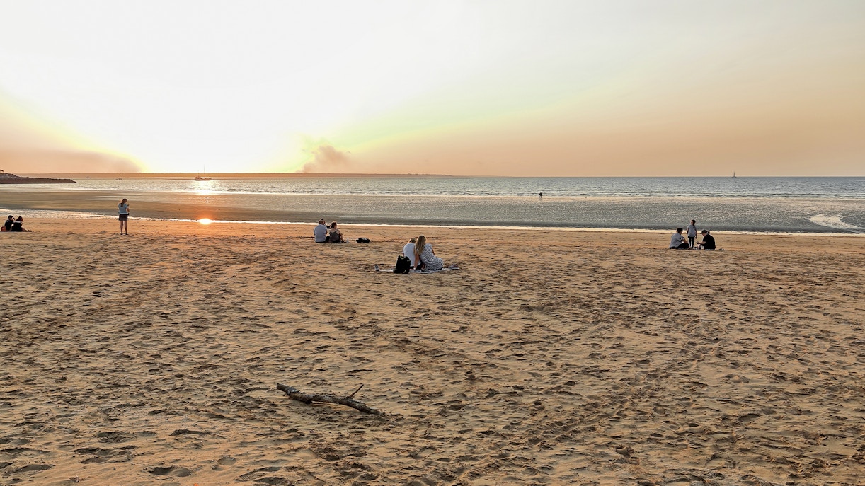 People enjoying sunset at Mindil Beach, Darwin, with sailboats on the horizon.