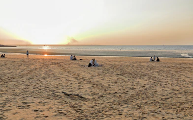 People enjoying sunset at Mindil Beach, Darwin, with sailboats on the horizon.