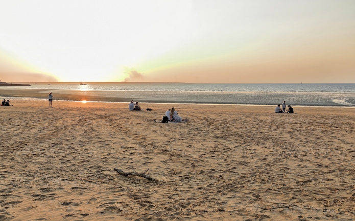 People enjoying sunset at Mindil Beach, Darwin, with sailboats on the horizon.
