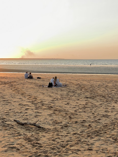 People enjoying sunset at Mindil Beach, Darwin, with sailboats on the horizon.