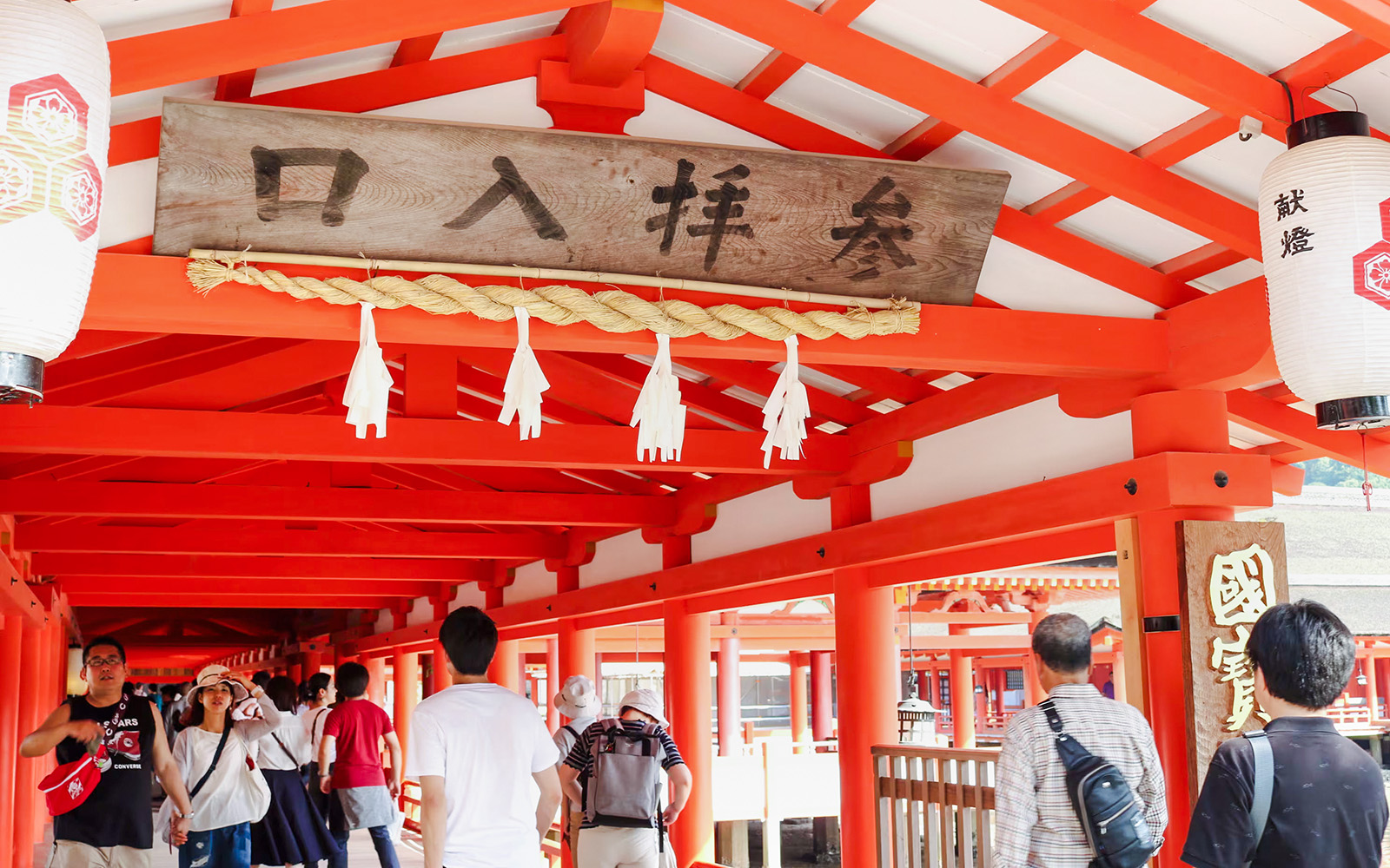 Visitors walking through the vibrant red corridors of Itsukushima Shrine, Japan.