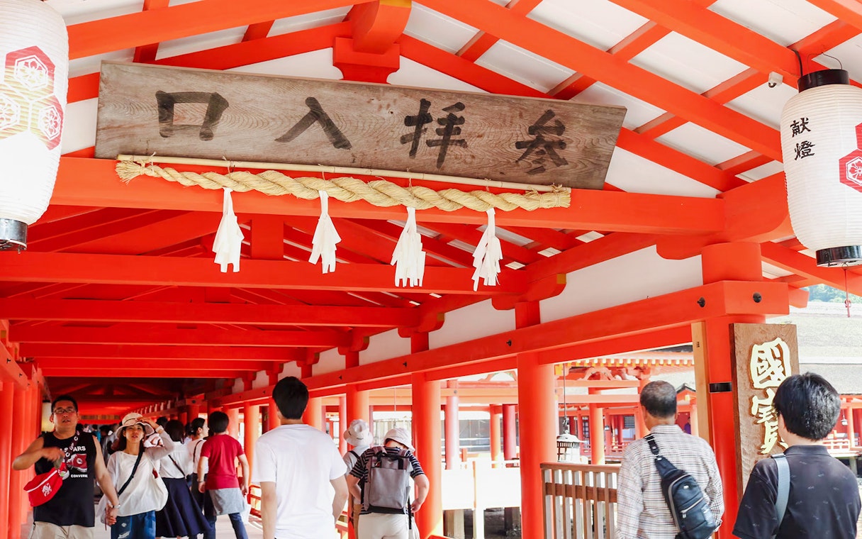 Visitors walking through the vibrant red corridors of Itsukushima Shrine, Japan.