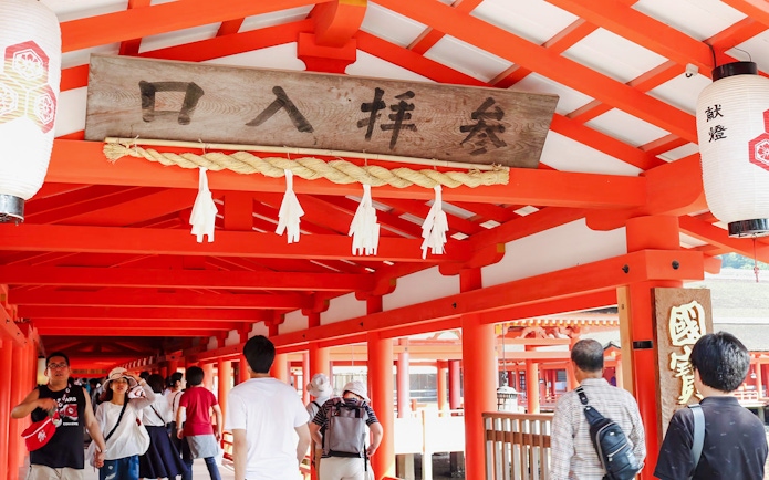 Visitors walking through the vibrant red corridors of Itsukushima Shrine, Japan.
