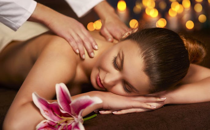 Woman receiving a back massage at Mandala Day Spa with a pink lily nearby.