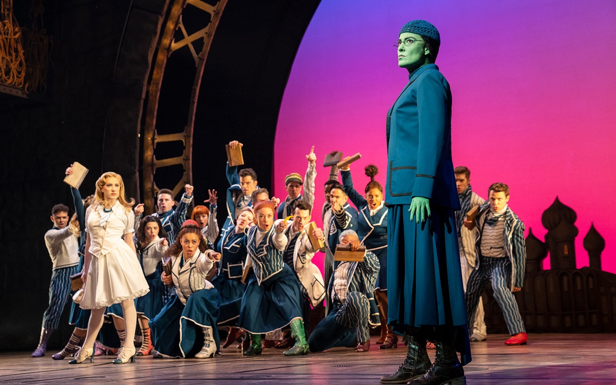 Stage scene from the musical Wicked with characters in costume during a dramatic moment.