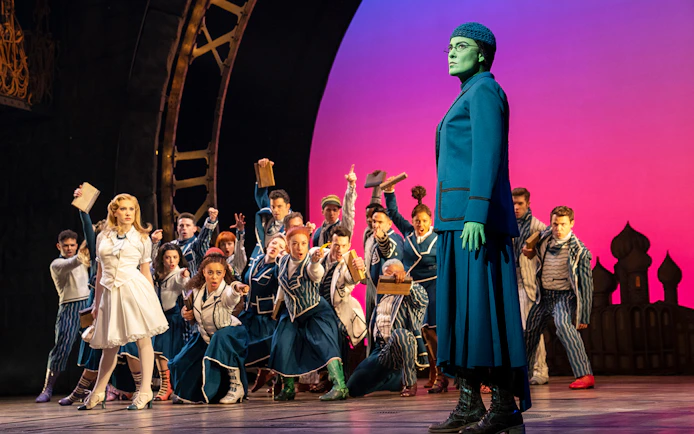 Stage scene from the musical Wicked with characters in costume during a dramatic moment.