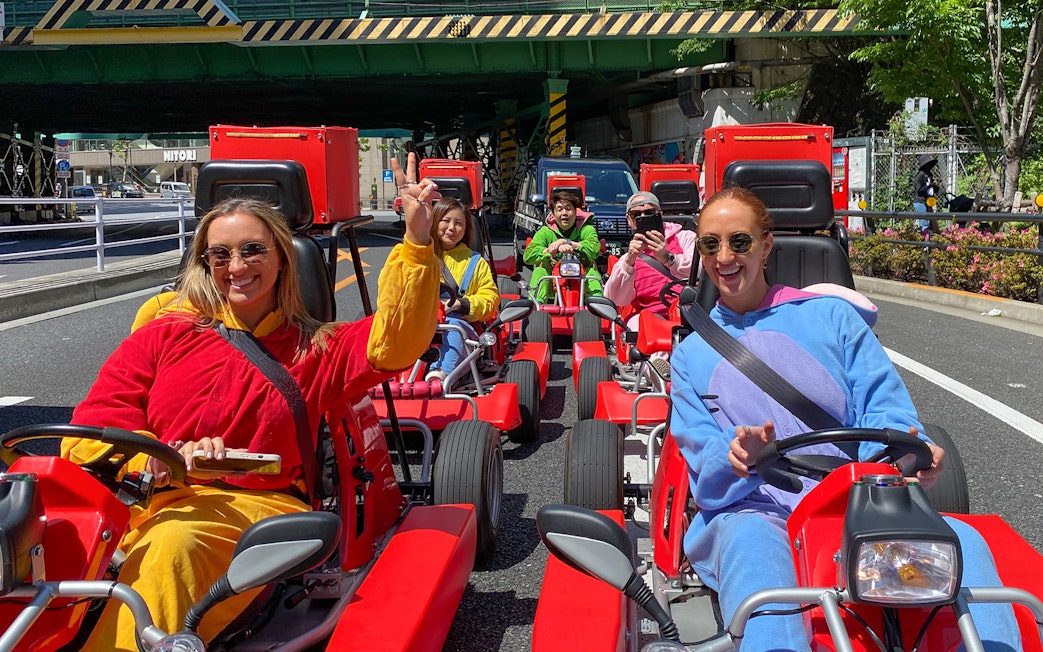 Participants driving go-karts in colorful outfits on a street in Shibuya, Tokyo.