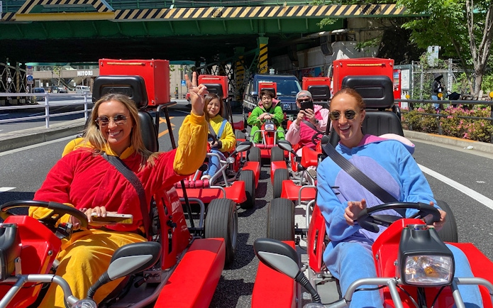 Participants driving go-karts in colorful outfits on a street in Shibuya, Tokyo.