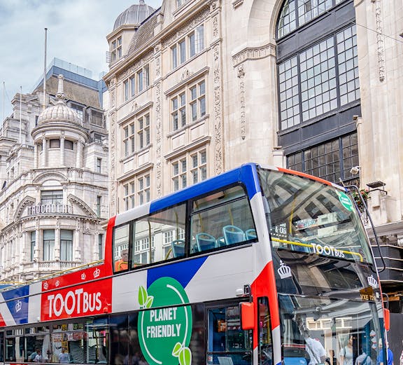 Tootbus double-decker bus in London with a planet-friendly design near historic buildings.