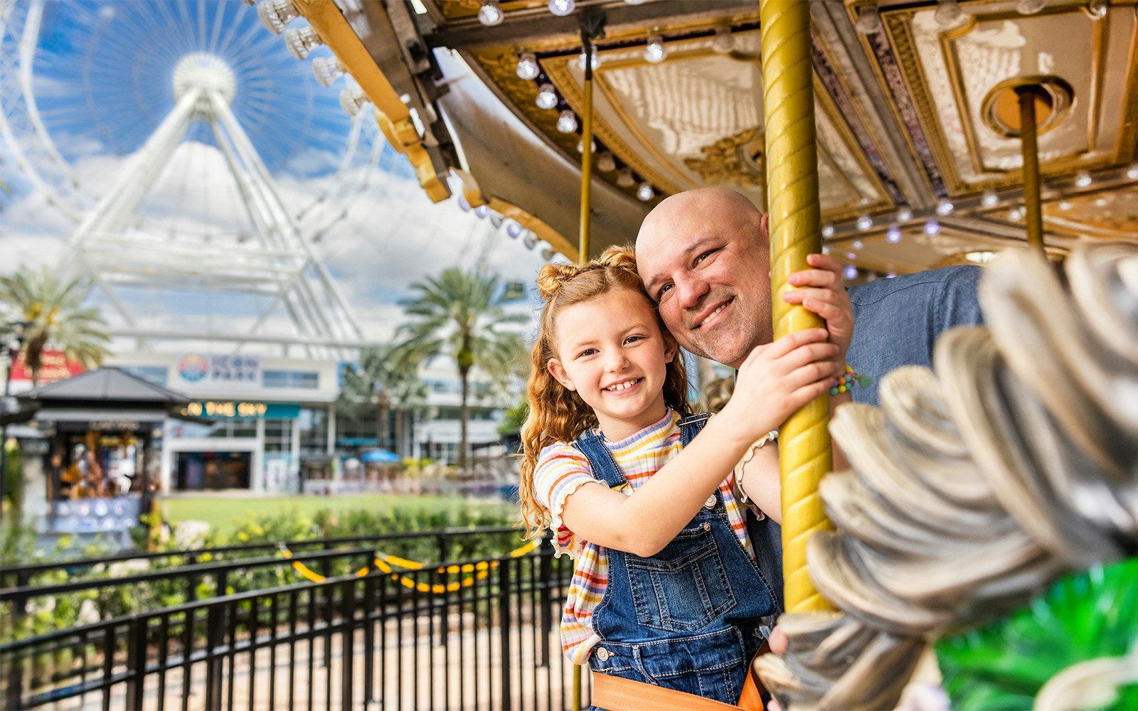 Father and daughter on a carousel at ICON Park, Orlando with The Wheel in the background.