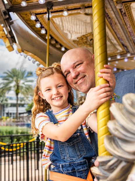 Father and daughter on a carousel at ICON Park, Orlando with The Wheel in the background.