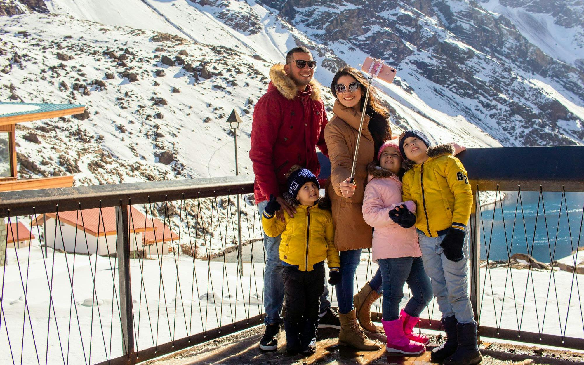 Family taking a selfie at snowy Portillo resort with mountains in the background.