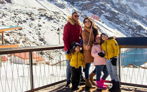 Family taking a selfie at snowy Portillo resort with mountains in the background.