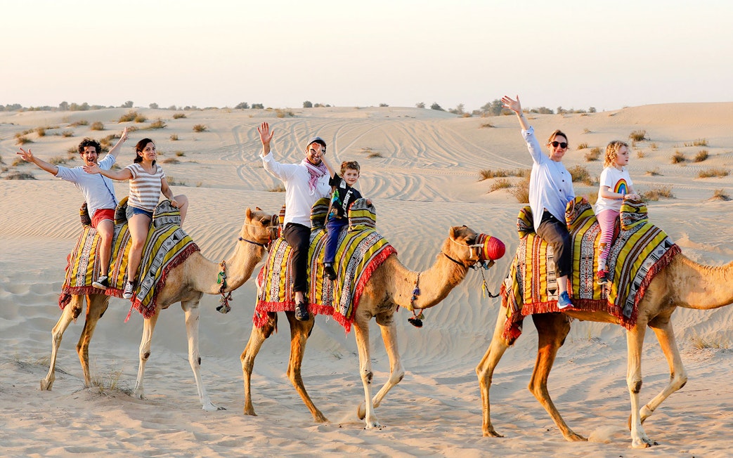 Camel ride in Abu Dhabi desert with tourists enjoying the safari experience.