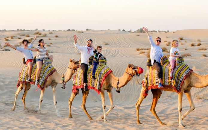 Camel ride in Abu Dhabi desert with tourists enjoying the safari experience.