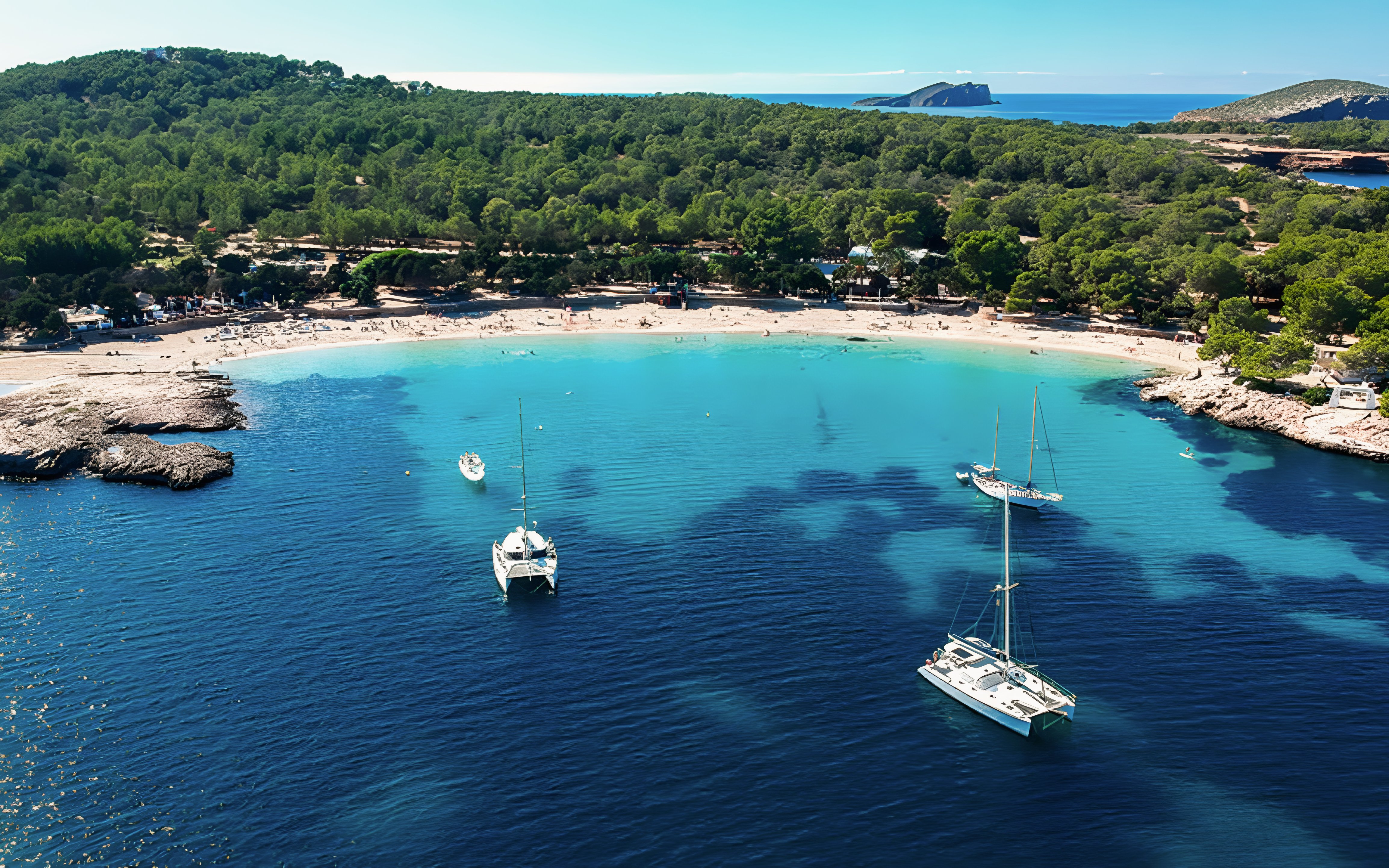 Aerial view of Cala Bassa Beach in Ibiza, Spain with boats in turquoise water.