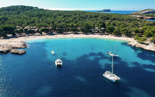 Aerial view of Cala Bassa Beach in Ibiza, Spain with boats in turquoise water.