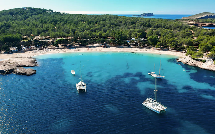 Aerial view of Cala Bassa Beach in Ibiza, Spain with boats in turquoise water.